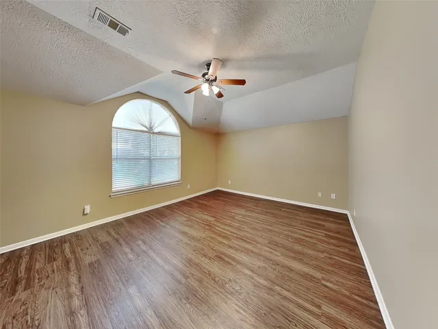 an empty room with wooden floor chandelier fan and windows