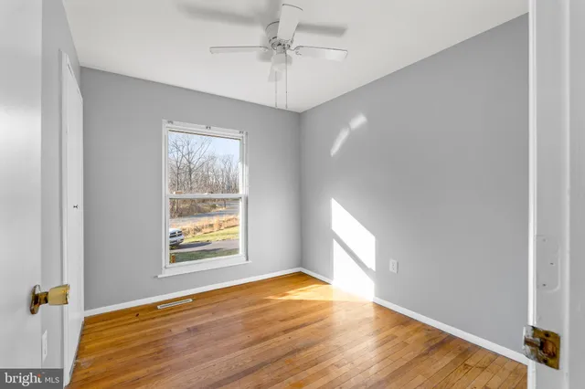 an empty room with wooden floor chandelier fan and windows