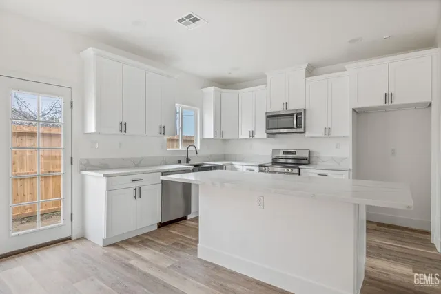 a kitchen with stainless steel appliances granite countertop white cabinets a sink a stove a refrigerator and microwave with wooden floor