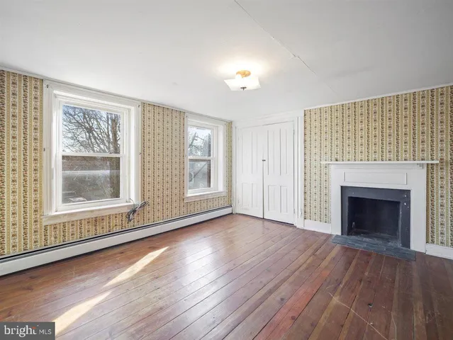 an empty room with wooden floor fireplace and windows