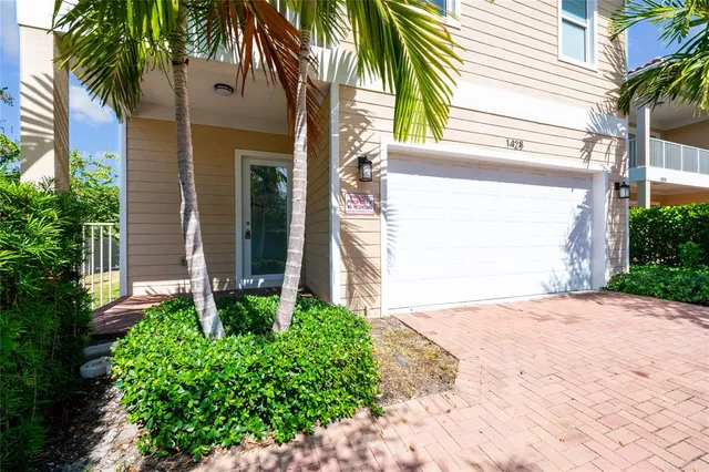 a view of yellow house with a small yard and potted plants