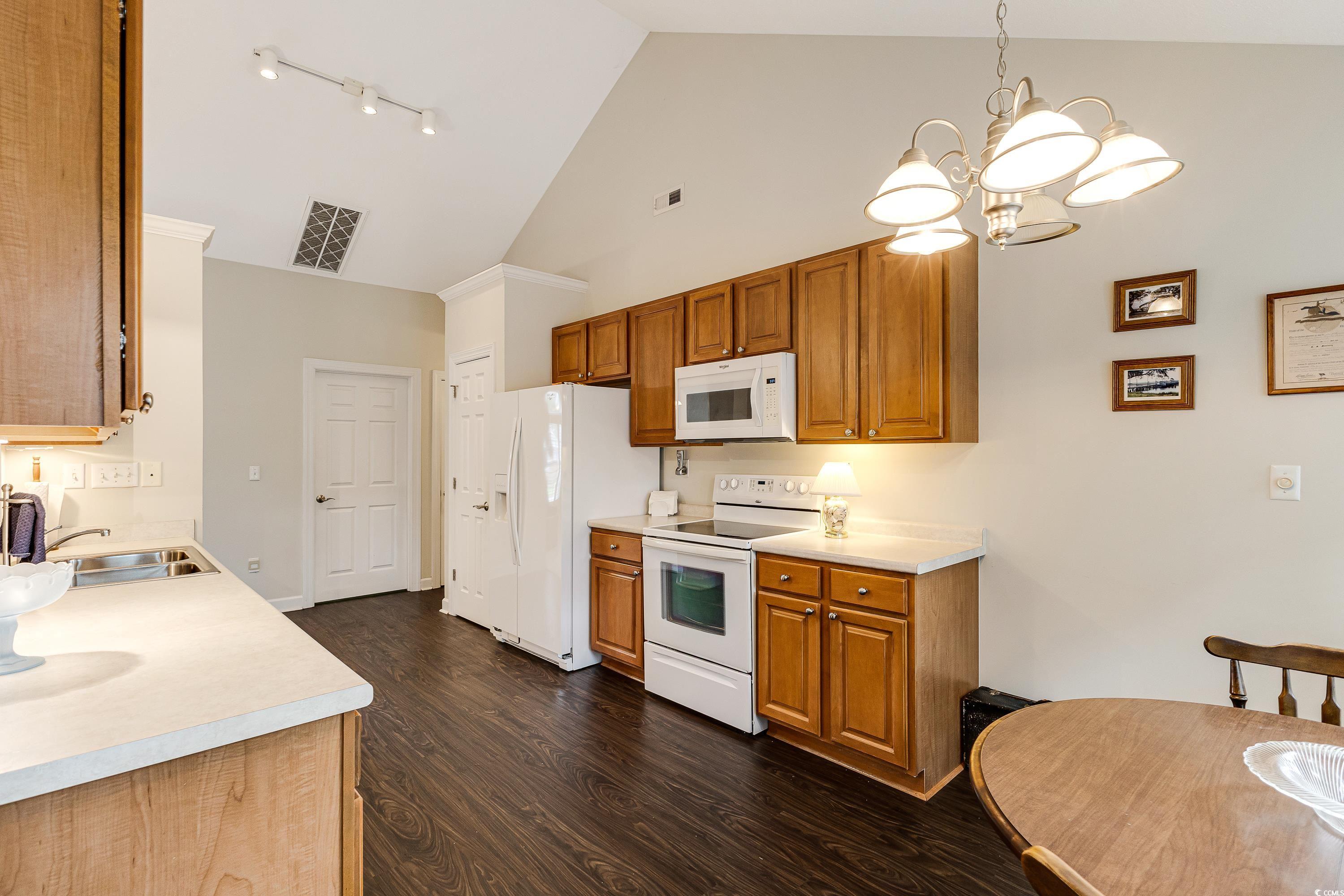101 Cedar Tree Lane Southwest Calabash, NC 28467 - Photo 16 of 40 Kitchen featuring high vaulted ceiling, white appliances, a chandelier, dark wood finished floors, and brown cabinets