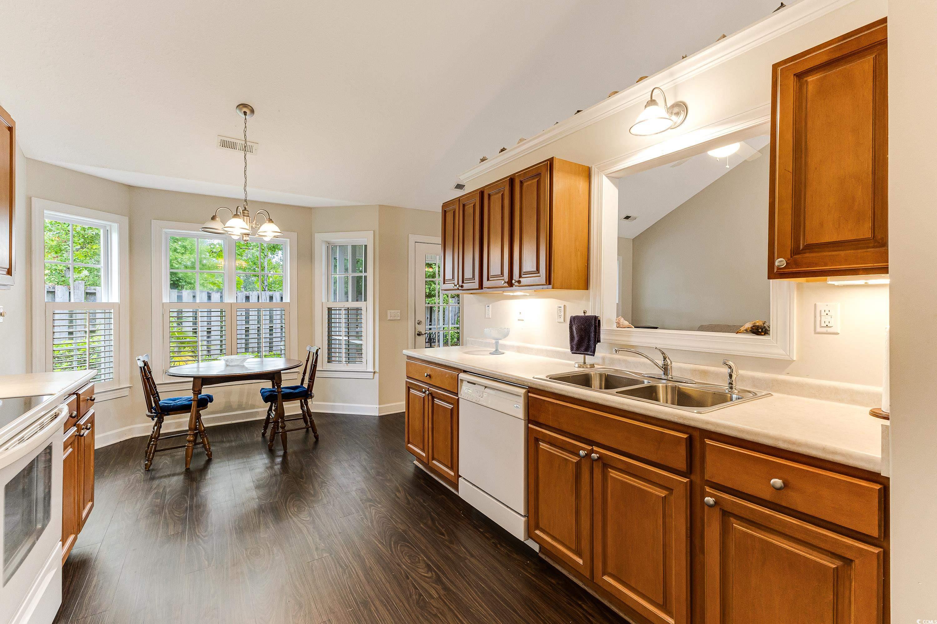 101 Cedar Tree Lane Southwest Calabash, NC 28467 - Photo 18 of 40 Kitchen with brown cabinets, light countertops, white appliances, dark wood-style flooring, and pendant lighting