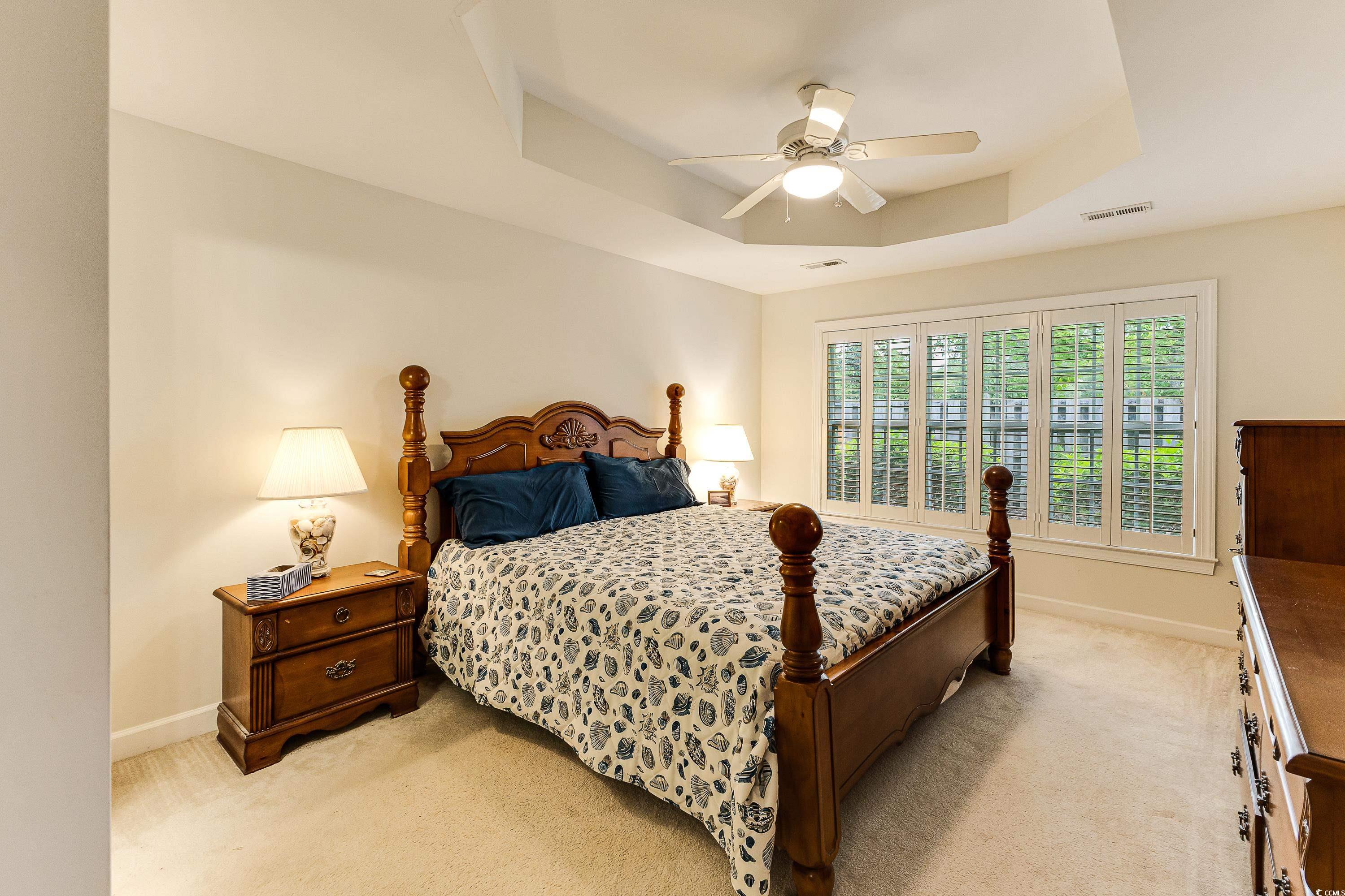 101 Cedar Tree Lane Southwest Calabash, NC 28467 - Photo 19 of 40 Bedroom featuring a tray ceiling, light carpet, and a ceiling fan