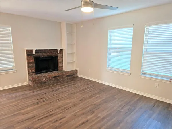 an empty room with wooden floor fireplace and windows