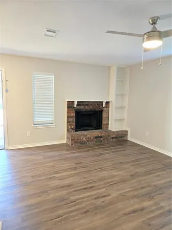 a view of an empty room with wooden floor fireplace and a window