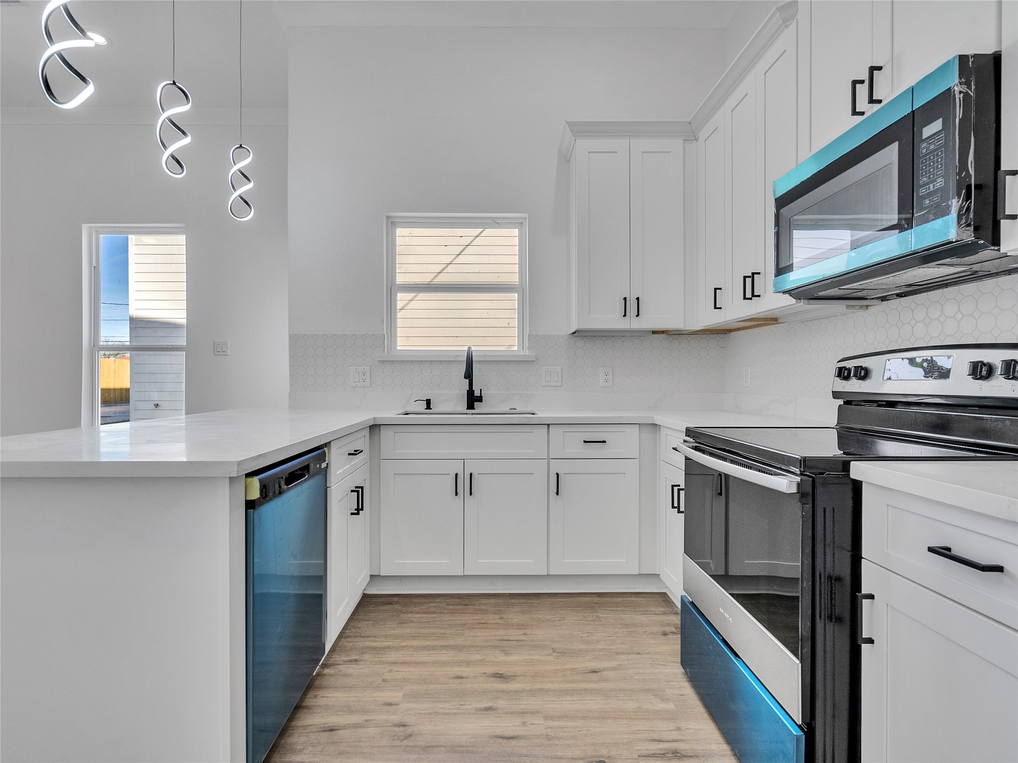 5126 Clover Street, Unit A/B Houston, TX 77033 - Photo 11 of 29 Modern kitchen with sleek white cabinetry and countertops, stainless steel appliances, and stylish pendant lighting. Bright and inviting with ample natural light and a functional layout.