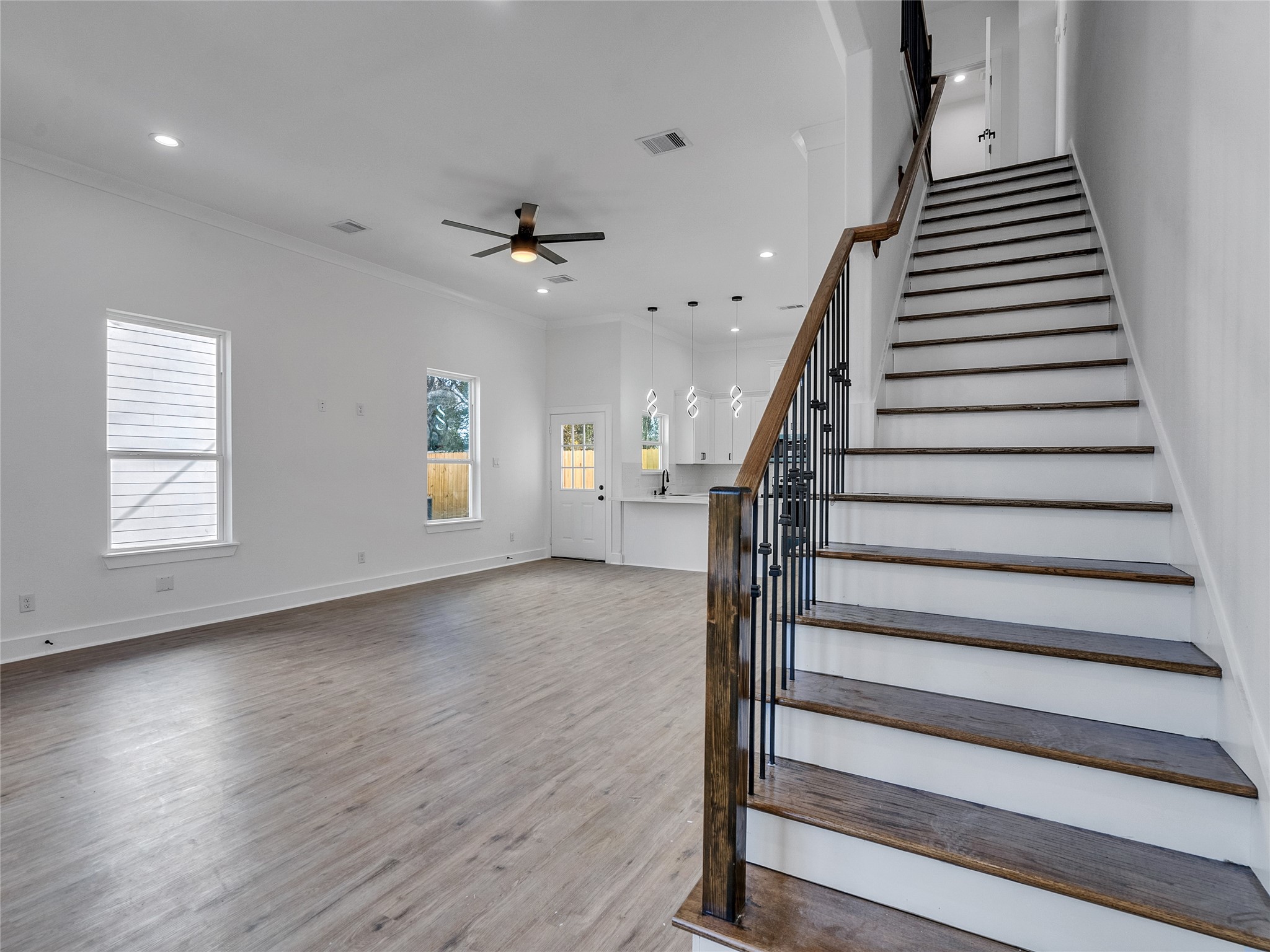 5126 Clover Street, Unit A/B Houston, TX 77033 - Photo 6 of 29 This photo showcases a spacious, open-concept living area with modern wood flooring and a sleek staircase. The space is bright, featuring large windows and recessed lighting. The kitchen is visible in the background, accented by contemporary pendant lights.
