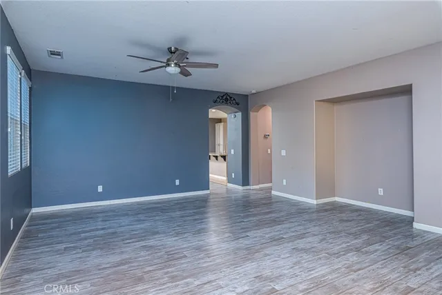 a view of an empty room with wooden floor and a ceiling fan