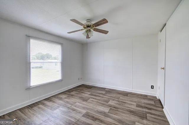 a view of empty room with wooden floor and fan