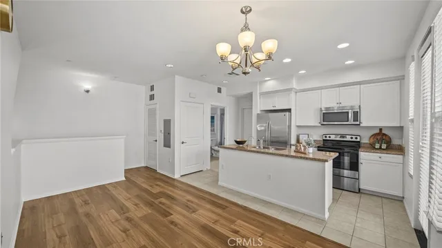 a kitchen with stainless steel appliances granite countertop a refrigerator a stove oven a sink dishwasher and white cabinets with wooden floor