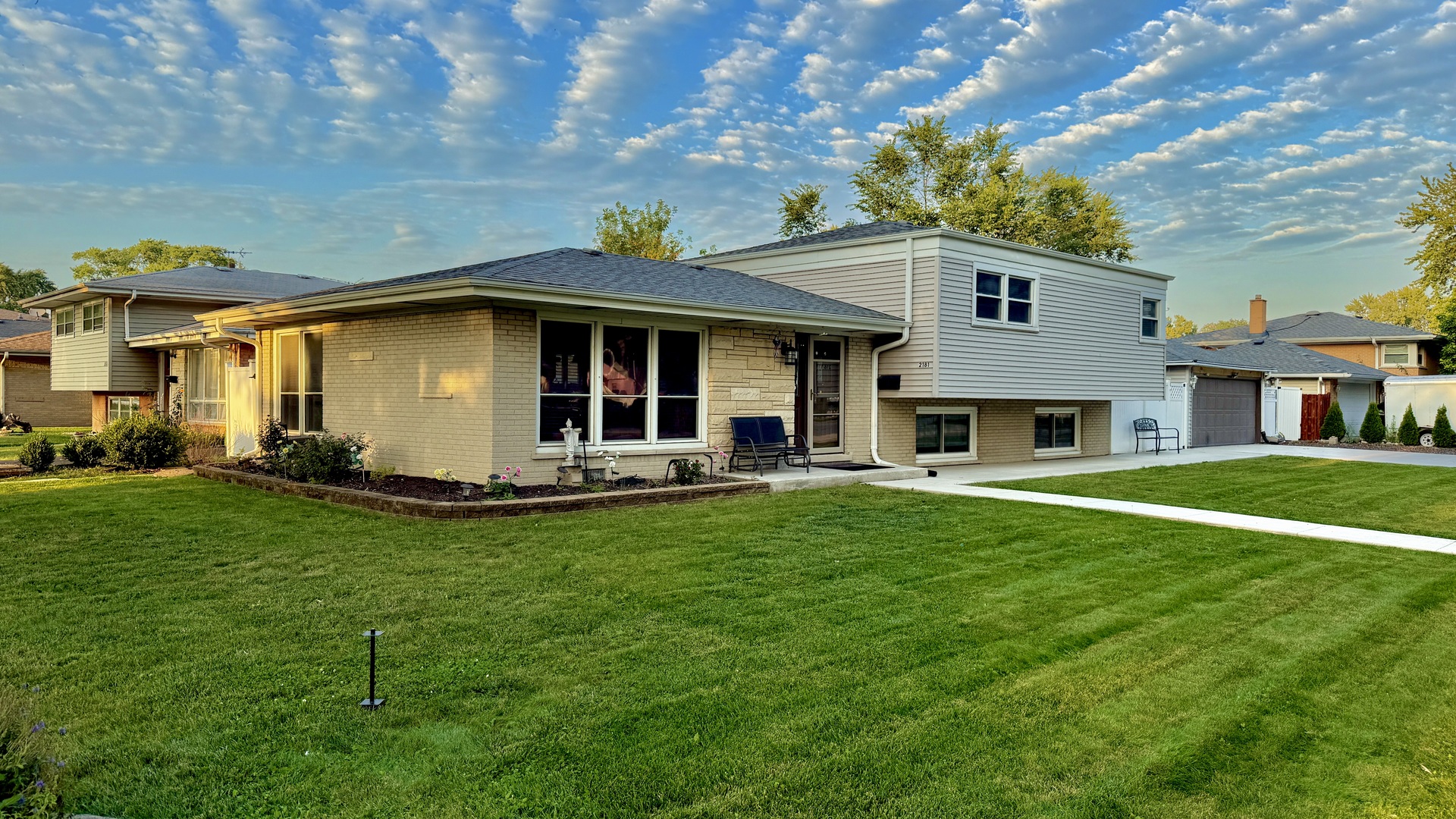 a view of a white house in front of a big yard with plants and large trees