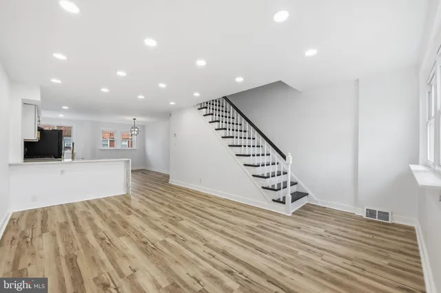 a view of an empty room with wooden floor staircase and a kitchen