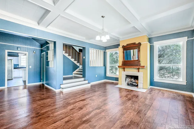 an empty room with fireplace wooden floor chandelier and windows