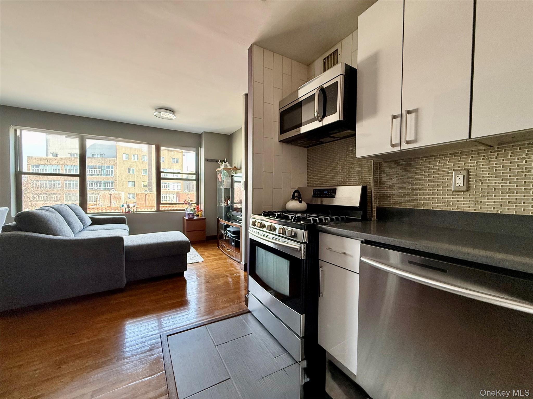 87-14 57th Road, Unit 5A Queens, NY 11373 - Photo 6 of 34 a kitchen with stainless steel appliances granite countertop a sink dishwasher a stove top oven a dining table and chairs with wooden floor
