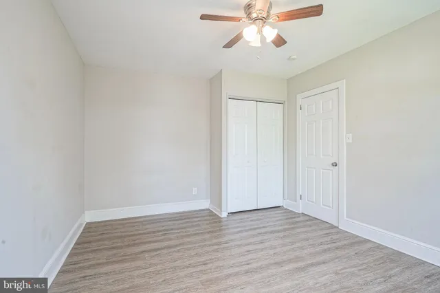 a view of an empty room with wooden floor and a ceiling fan