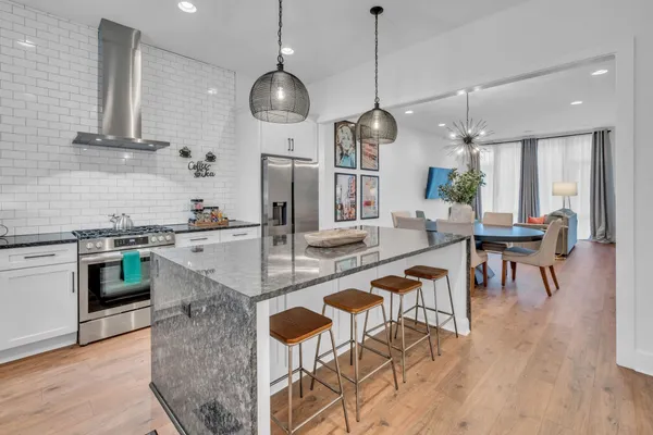 a open kitchen with stainless steel appliances granite countertop a stove top oven a refrigerator a kitchen island a dining table and chairs with wooden floor