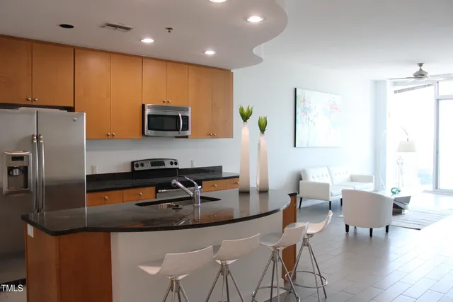 a kitchen with stainless steel appliances granite countertop a stove a refrigerator a kitchen island a dining table and chairs