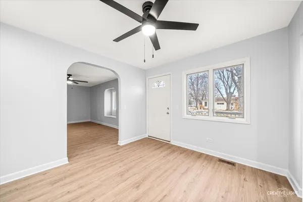 a view of an empty room with wooden floor and a ceiling fan