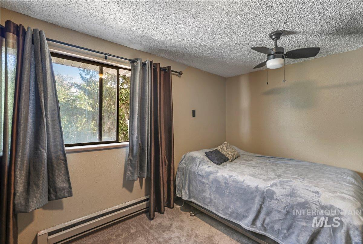 259 Pheasant Road West, Unit 2 Twin Falls, ID 83301 - Photo 22 of 31 Bedroom featuring baseboard heating, carpet flooring, a textured ceiling, a textured wall, and a ceiling fan