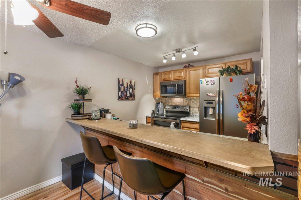 259 Pheasant Road West, Unit 2 Twin Falls, ID 83301 - Photo 4 of 31 Kitchen with appliances with stainless steel finishes, backsplash, light wood-style flooring, a kitchen breakfast bar, and a textured ceiling