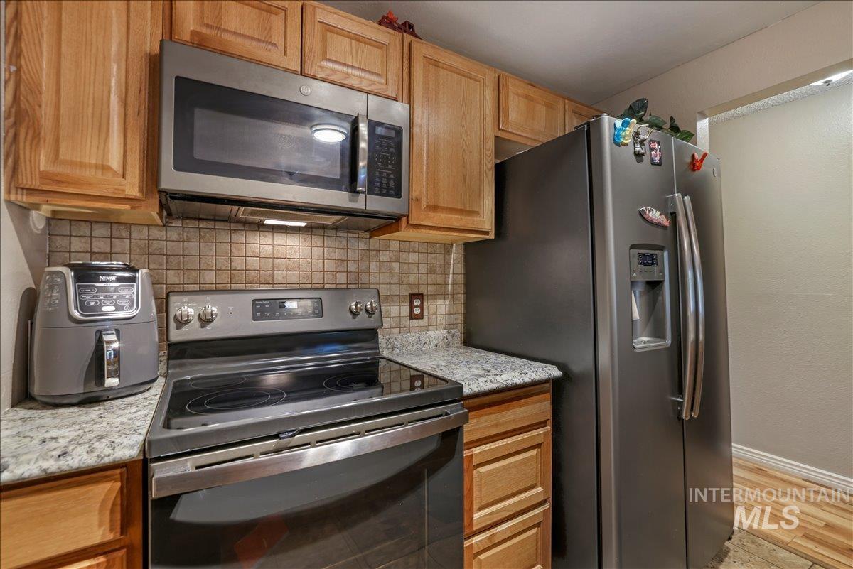 259 Pheasant Road West, Unit 2 Twin Falls, ID 83301 - Photo 5 of 31 Kitchen with appliances with stainless steel finishes, backsplash, light stone counters, and light wood-style flooring