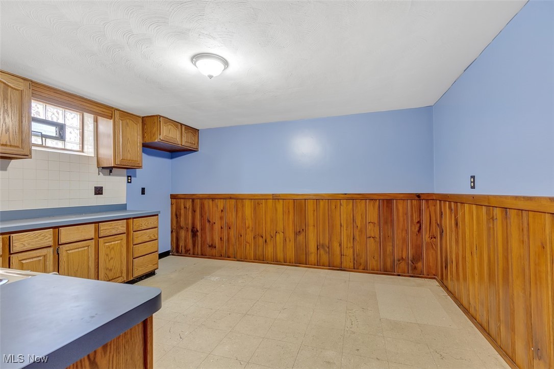6136 Ridge Road Cleveland, OH 44129 - Photo 32 of 40 Kitchen with a wainscoted wall, wood walls, light flooring, brown cabinets, and backsplash