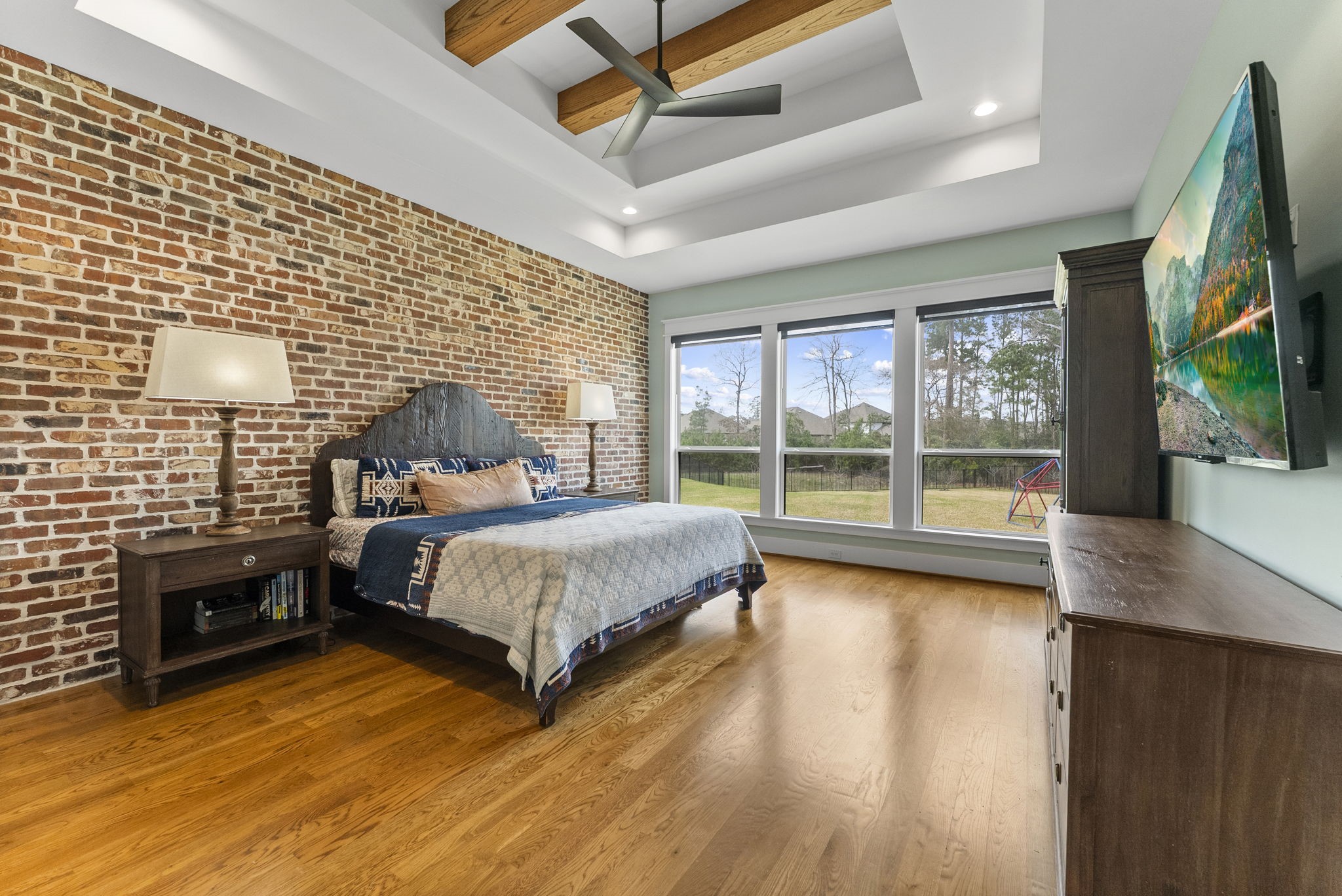 14019 Beartooth Bend Trail Conroe, TX 77384 - Photo 14 of 28 Generous primary suite highlighted by a striking brick accent wall, expansive windows overlooking the backyard, a tray ceiling with wood beams, and an abundance of natural light.