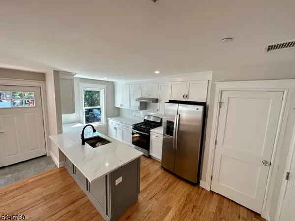 a kitchen with stainless steel appliances granite countertop a refrigerator a sink a stove and a wooden floors