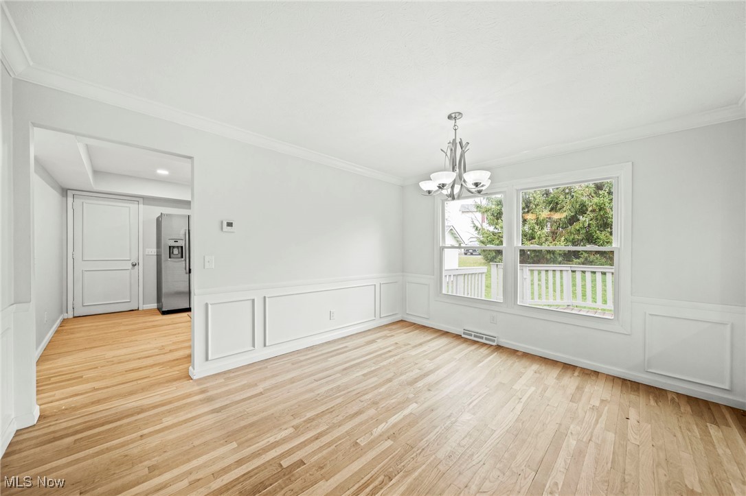 91 Paradise Road Painesville, OH 44077 - Photo 9 of 39 Spare room with ornamental molding, light wood-style flooring, a chandelier, a decorative wall, and wainscoting