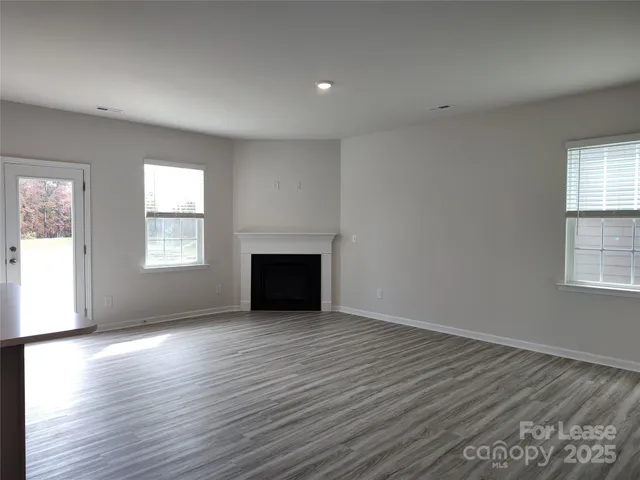 an empty room with wooden floor fireplace and windows