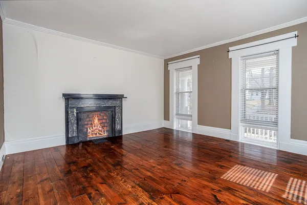 an empty room with wooden floor fireplace and windows