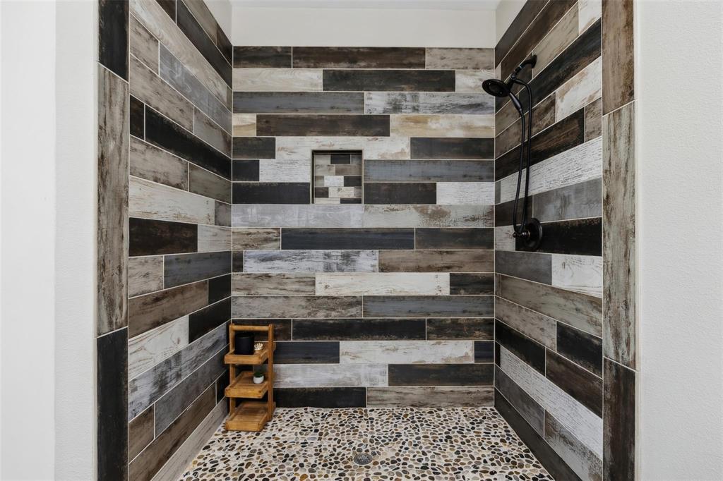 4662 Barbara Road River Oaks, TX 76114 - Photo 10 of 14 Shower stall featuring wood-finish wall tiling, pebble floor, built-in shower niche, and a matte black shower fixture