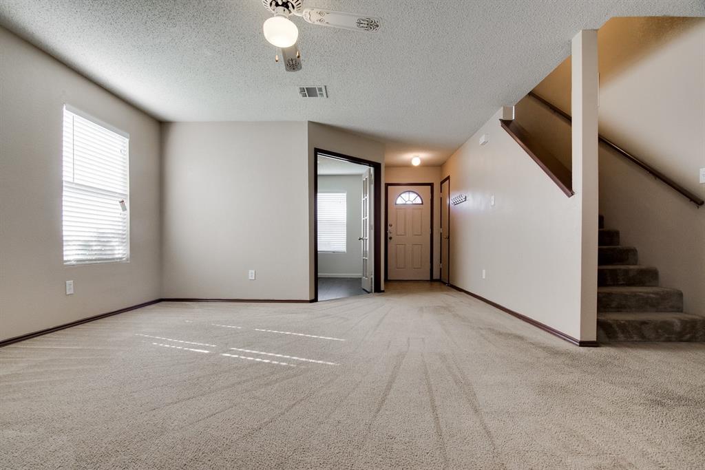 8211 Leaning Oak Court Arlington, TX 76002 - Photo 9 of 26 Unfurnished living room featuring plenty of natural light, light colored carpet, a textured ceiling, stairway, and ceiling fan