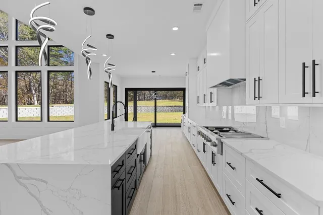 a large white kitchen with granite countertop a stove a sink a cabinets and wooden floor