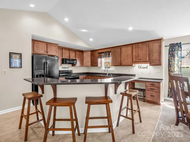 a kitchen with stainless steel appliances granite countertop a stove top oven a refrigerator a sink and a dining table with white cabinets