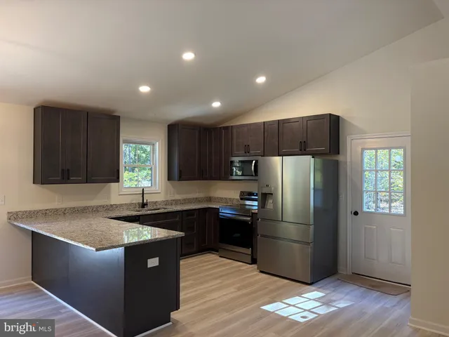 a kitchen with stainless steel appliances granite countertop a refrigerator a sink a stove a microwave and wooden cabinets