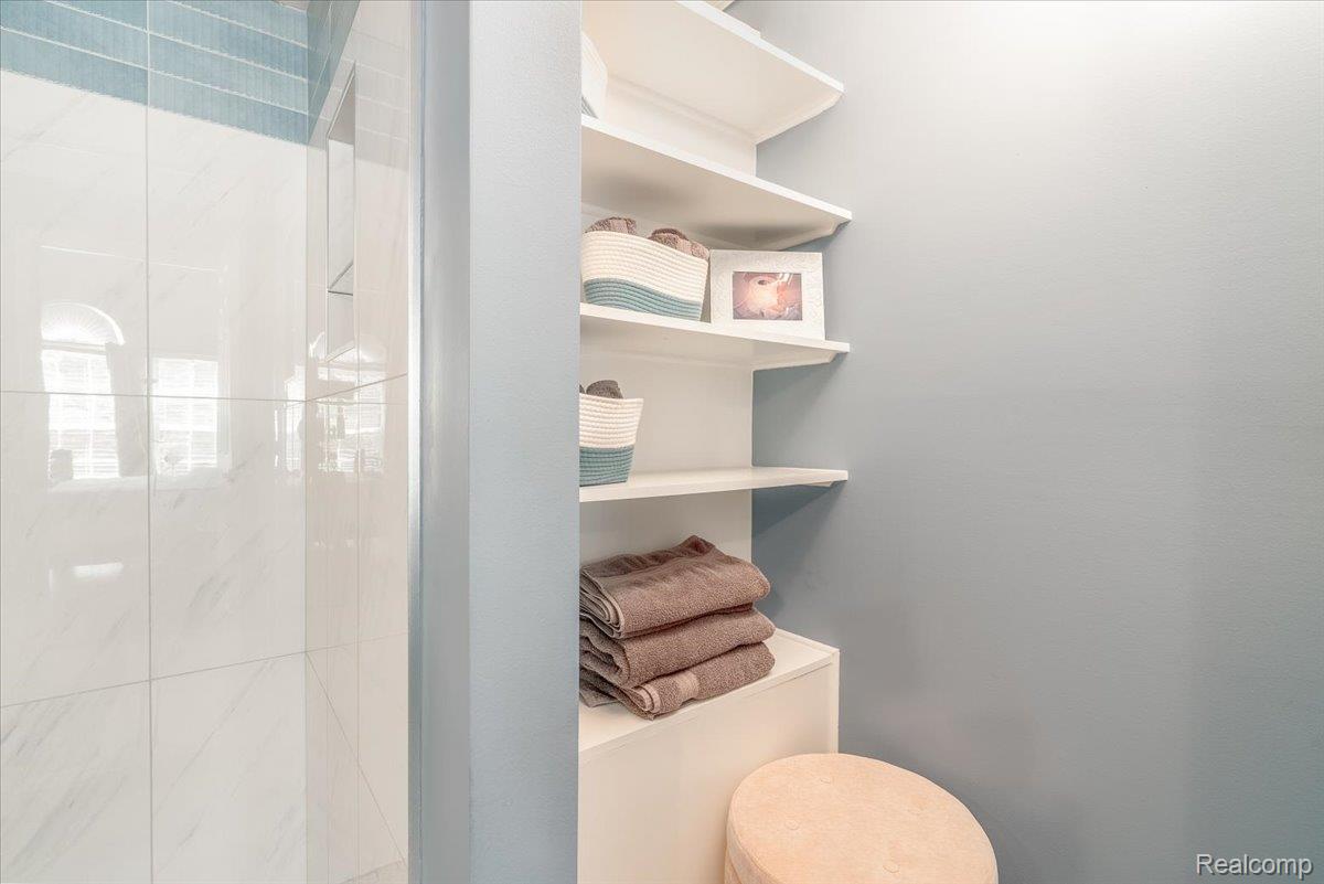49105 Hawksburry Road Canton, MI 48188 - Photo 23 of 51 Built-in shelving unit with multiple white shelves, white shower tiling, and a blue decorative tile accent