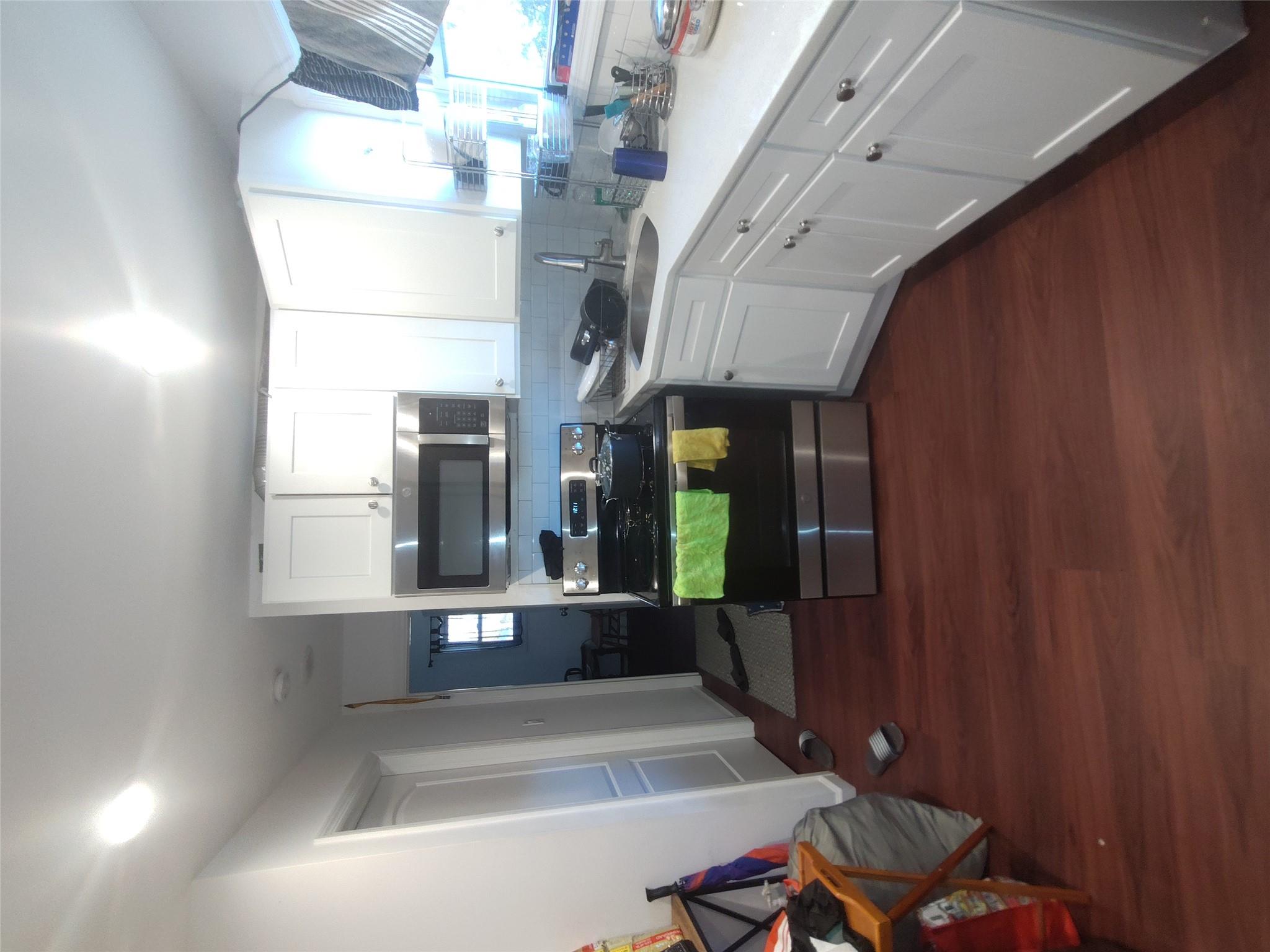 2167 A Great Neck Road Copiague, NY 11726 - Photo 10 of 18 Kitchen featuring stainless steel electric range oven, decorative backsplash, dark wood-style flooring, white cabinets, and light countertops