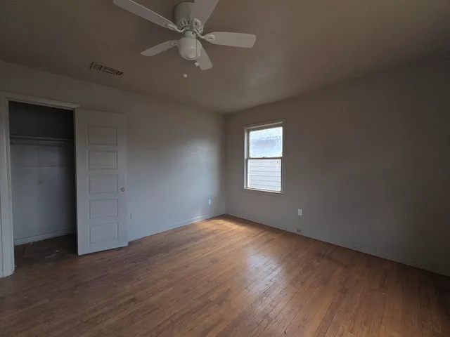 an empty room with wooden floor fan and windows