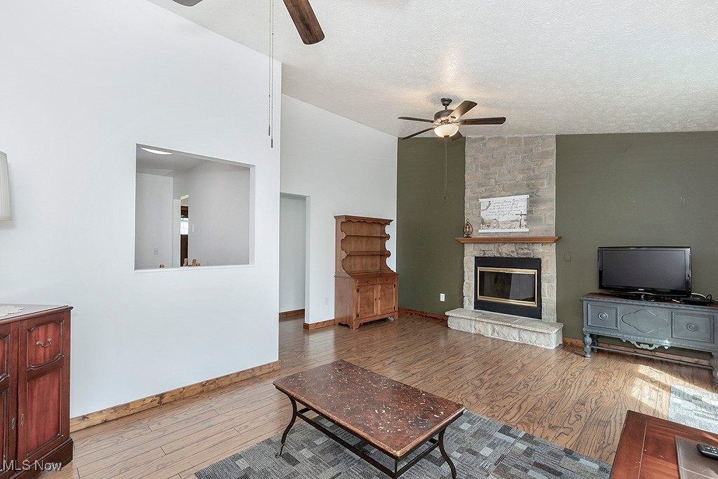 6881 Lake Road Medina, OH 44256 - Photo 4 of 34 Living room featuring a stone fireplace, vaulted ceiling, a textured ceiling, a ceiling fan, and wood finished floors