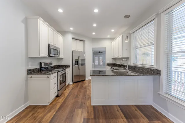 a kitchen with stainless steel appliances granite countertop a refrigerator a sink dishwasher a stove and white countertops with wooden floor