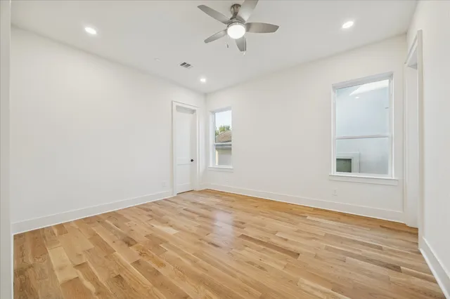an empty room with wooden floor ceiling fan and windows