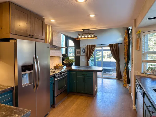 a kitchen with stainless steel appliances granite countertop a refrigerator a sink dishwasher a stove and a dining table with wooden floor