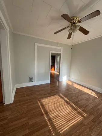 a view of an empty room with wooden floor and a ceiling fan