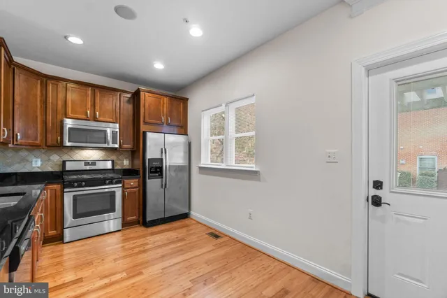 a kitchen with stainless steel appliances granite countertop a stove top oven a sink dishwasher a refrigerator and a microwave oven with wooden floor