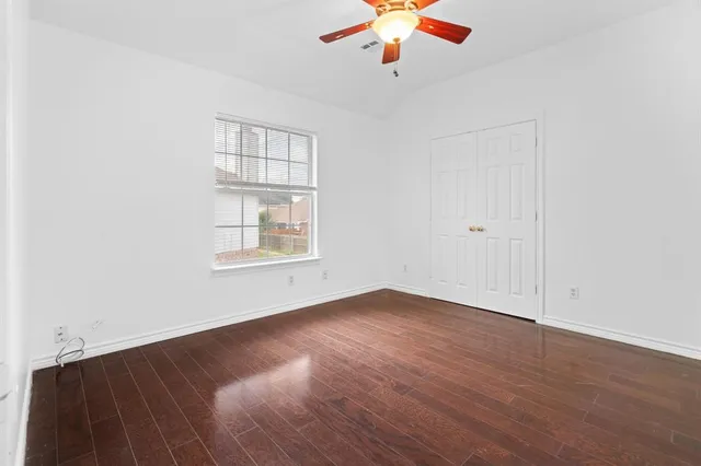 an empty room with wooden floor chandelier fan and windows