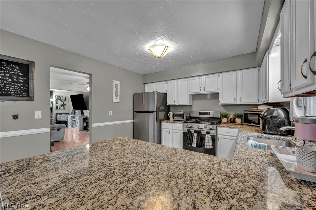 13800 Milo Road Garfield Heights, OH 44125 - Photo 10 of 39 Kitchen featuring stainless steel appliances, light stone counters, white cabinetry, ceiling fan, and a peninsula