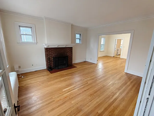 a view of an empty room with wooden floor fireplace and a window