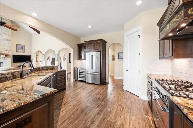 a kitchen with stainless steel appliances granite countertop a refrigerator a stove and a sink with wooden floors